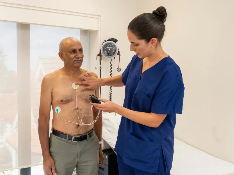 Technologist fitting a Holter monitor and chest electrodes on a patient